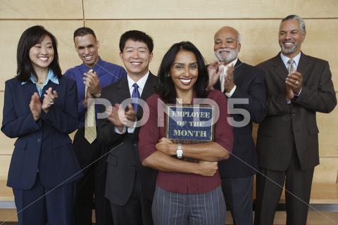 Stock photo of Businesswoman holding Employee of the Month plaque with co-workers applauding