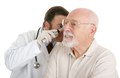 Senior man having his ears checked at the doctors office. Isolated on white.