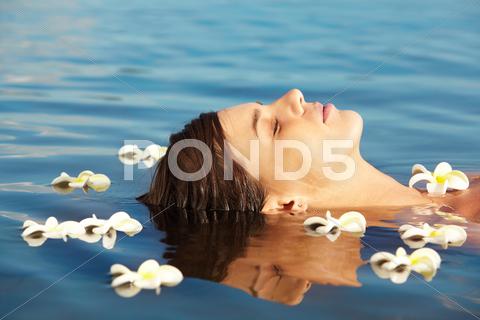 Close-Up Of Peaceful Female Face Above Water Surrounded By Plumeria Flowers