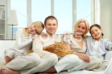 A Young Family With Son And Daughter Sitting On Sofa, Looking At Camera And Smil