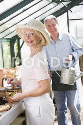 Woman In Greenhouse Planting Seeds And Man Holding Watering Can Smiling