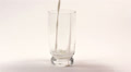 Milk flowing in transparent cup on white background Video