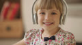 Pretty little girl in headphones waving her hand and smiling at camera