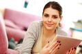 young beautiful woman lie on the couch and holding tablet computer at home