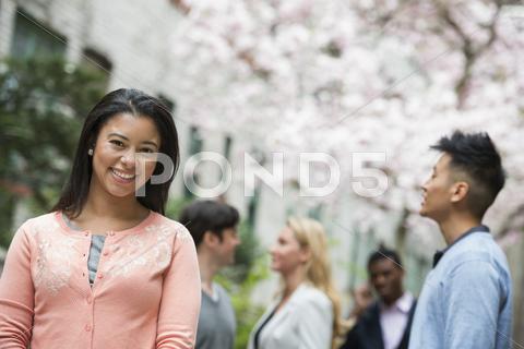 City Life In Spring. Young People Outdoors In A City Park. A Woman In A Pink
