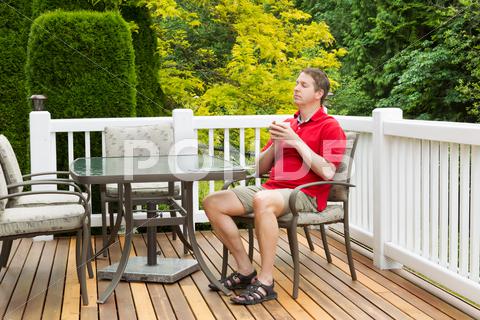 Mature Man Resting In Chair On Outdoor Patio With Cup Of Coffee In His Hands