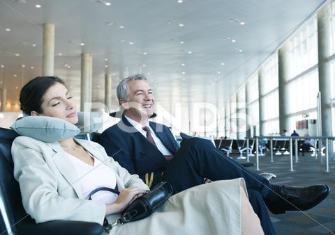 Business Travelers Sitting In Airport Lounge, Woman Napping With Neck Pillow