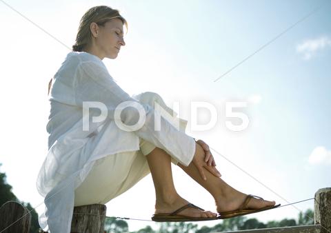 Woman Sitting On Top Of Fence, Low Angle View
