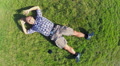 Young smiling male lies on grass, aerial vertical shot, zoom-out Video