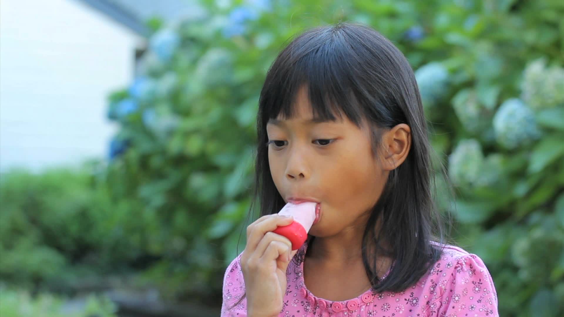 A cute little 6 year old Asian girl enjoys a delicious popsicle during the ...